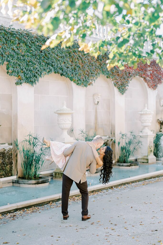 Andrea and Rich framed by golden trees and classic stone architecture.