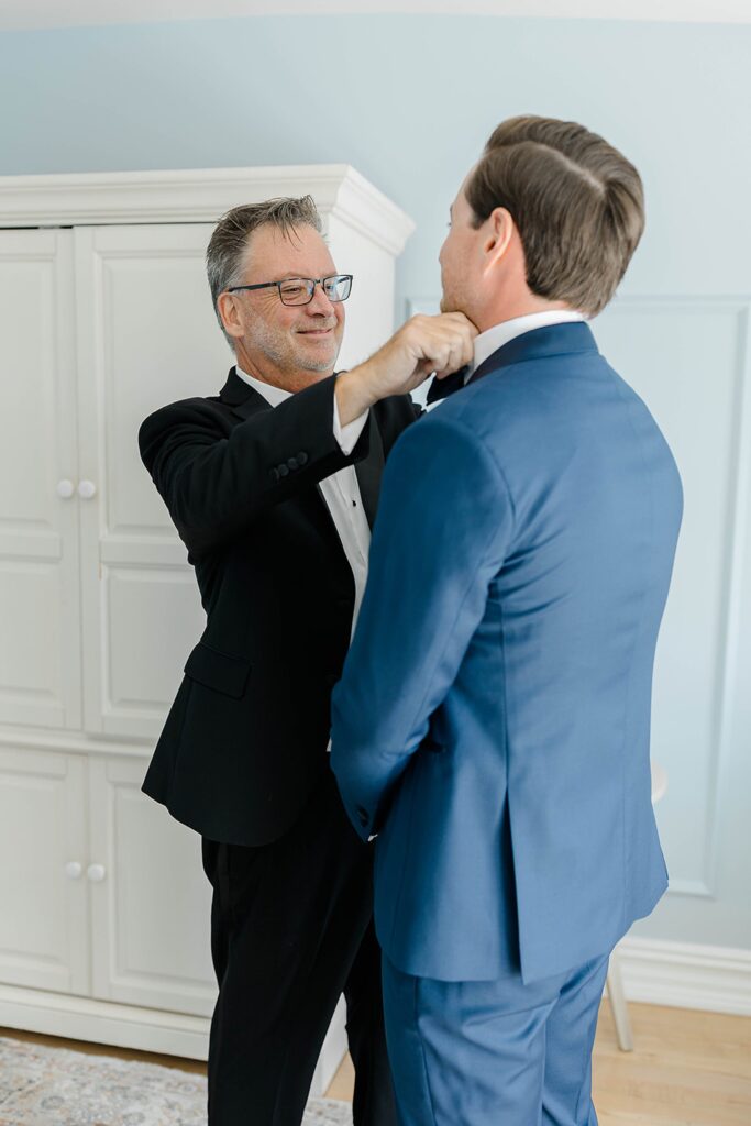 Groom adjusting tie with groomsmen in preparation for ceremony