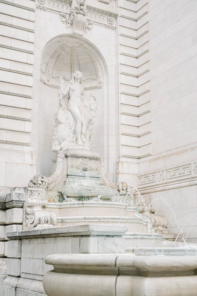 Close detail of Stefanie’s engagement ring held against the textured stone of New York Public Library architecture.
