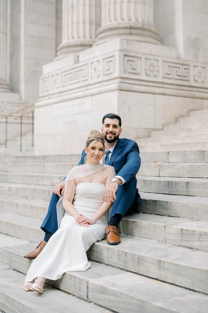 Editorial engagement portrait of Stefanie and Giovanni on the iconic New York Public Library steps against classic Beaux-Arts architecture.