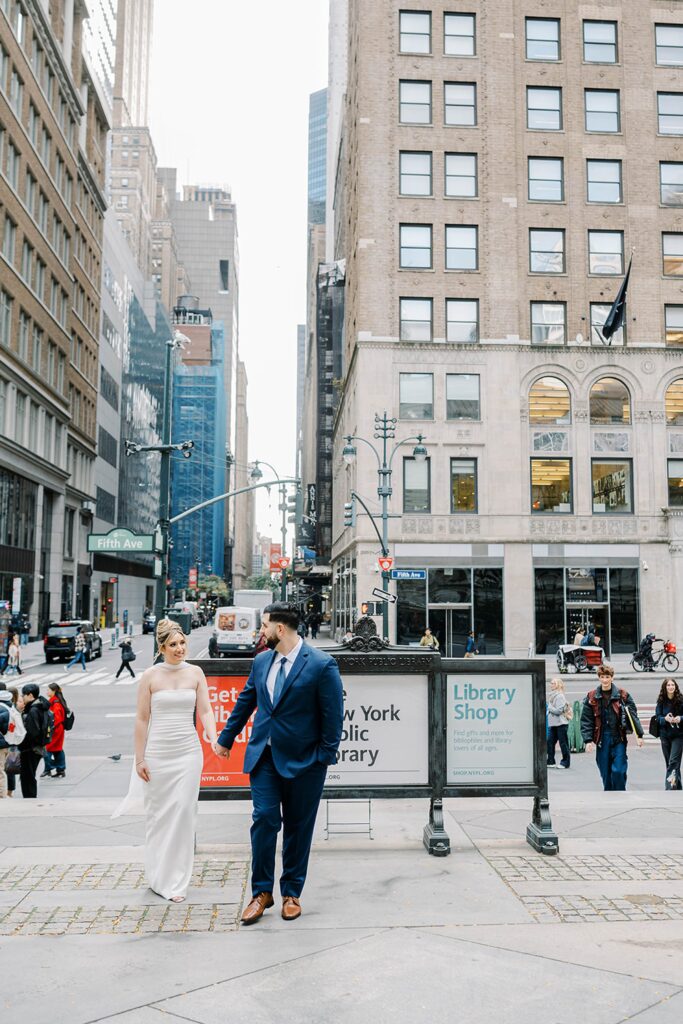 Stefanie and Giovanni walk hand-in-hand near the New York Public Library entrance, capturing movement and connection in NYC.